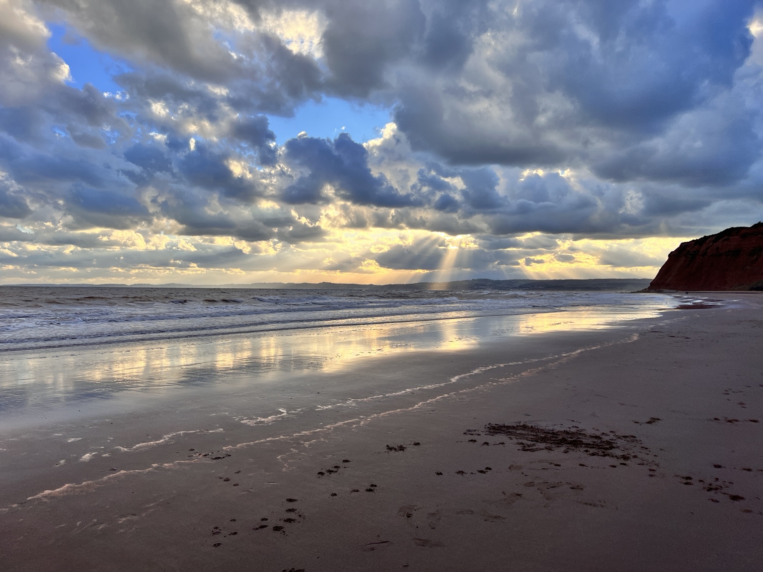 Waves meeting wet sand that reflects golden sunbeams on the Devon coast