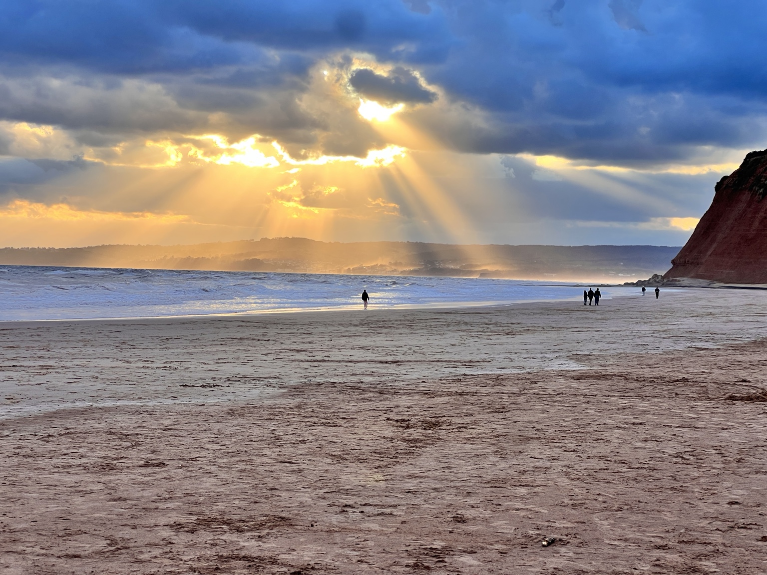 Golden sunbeams over the sandy Devon Cliffs beach beside high red cliffs
