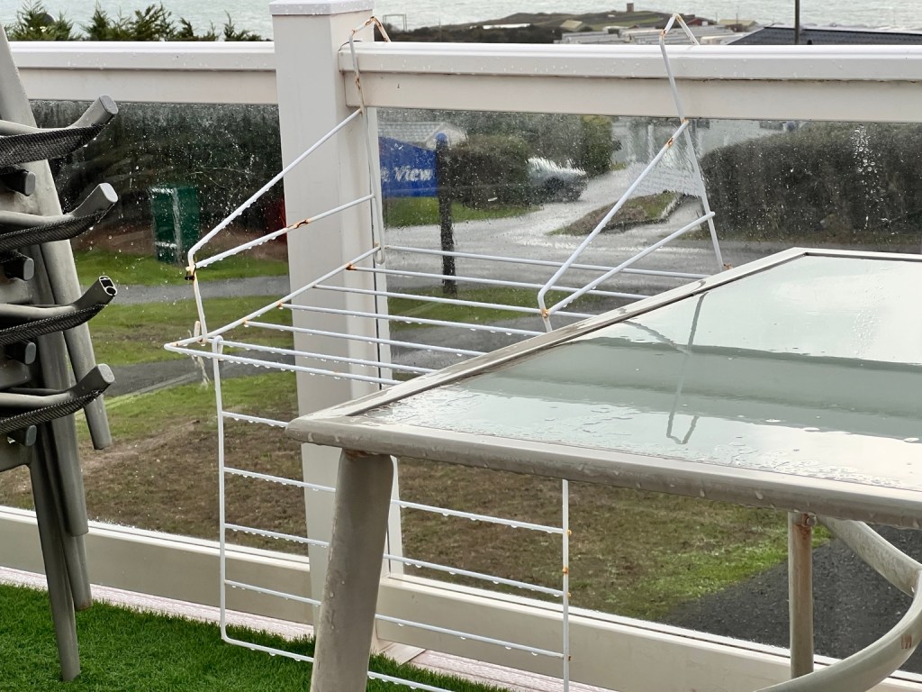 Rainwater on a glass patio table and drying rack outside a caravan at Devon Cliffs